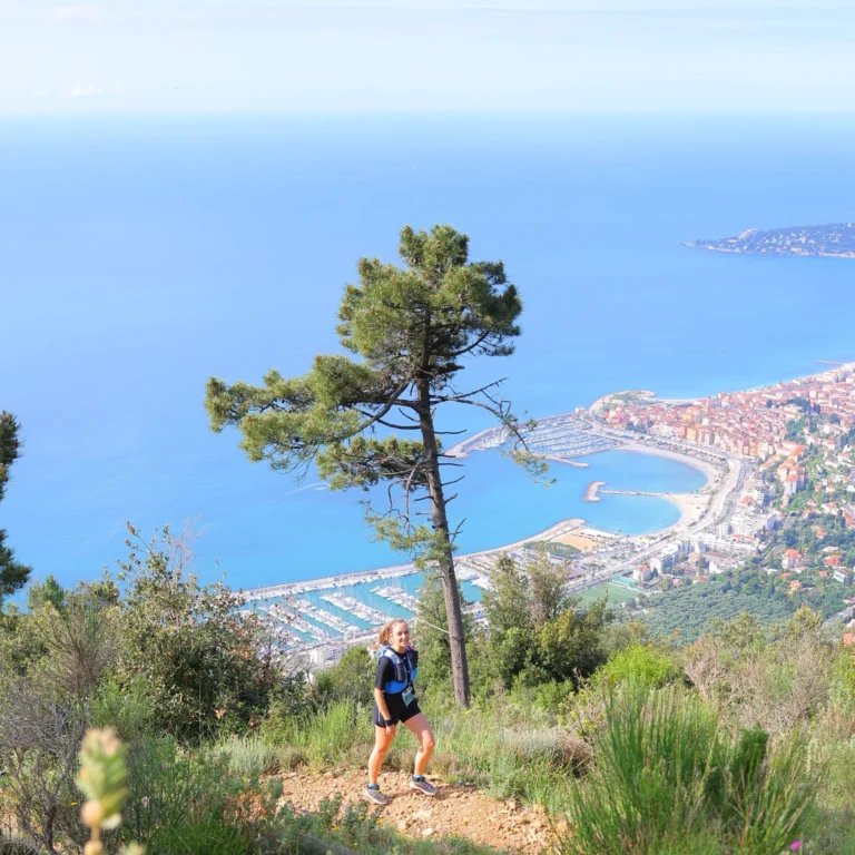 coureuse trail en train de gravir le Roc Orméa, ligne cotière de Menton à Monaco visible en arrière plan